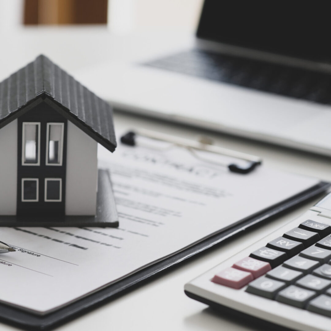 Pen and model house placed on contract documents with calculator and laptop, House construction contract signing concept.