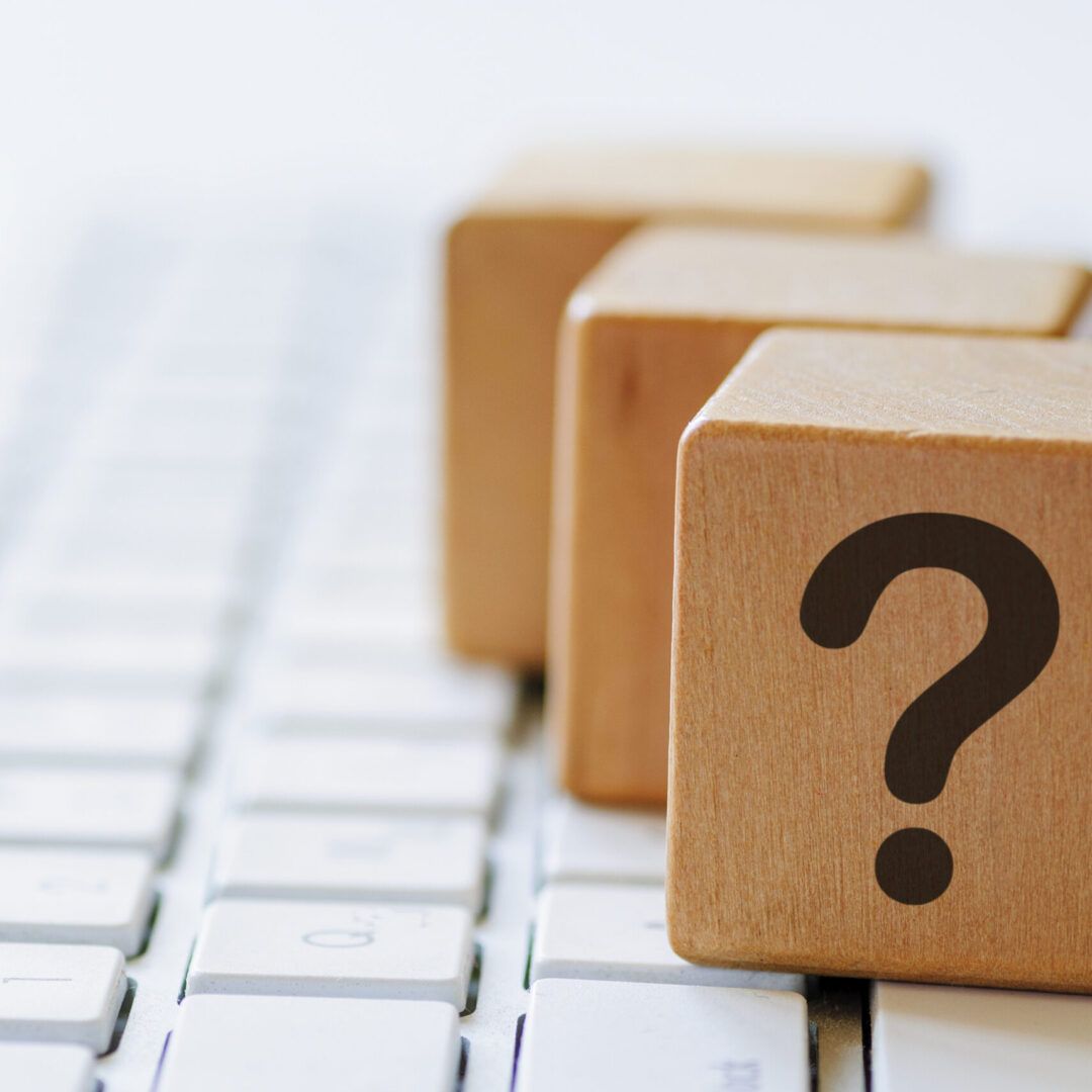 Small wooden dices with question mark on one side, sitting on computer keyboard and viewed in close-up with blurred copy space